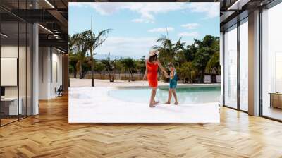 Happy biracial mother and daughter walking and holding hands by the swimming pool Wall mural