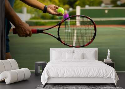 Midsection of biracial senior man holding racket serving tennis ball while playing at tennis court Wall mural