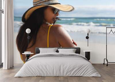 Mixed race woman on beach holiday using sunscreen cream Wall mural