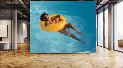 Mixed race woman sunbathing on inflatable in swimming pool Wall mural