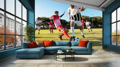 Multiracial players running and kicking the soccer ball during match in playground against clear sky Wall mural