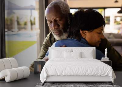 Multiracial senior man with eyes closed embracing woman while standing in nursing home Wall mural