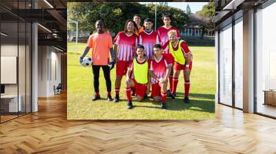 Portrait of cheerful male soccer team players in uniforms posing in playground during sunny day Wall mural