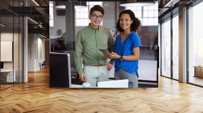 Portrait of diverse male and female colleague holding tablet and smiling standing in office Wall mural