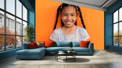 Portrait of happy biracial schoolgirl wearing t shirt over orange background at elementary school Wall mural