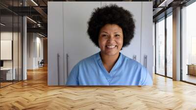 Portrait of smiling african american mid adult female nurse standing against cabinet in hospital Wall mural