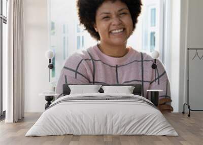 Portrait of smiling biracial young woman with afro hair and arms crossed standing against window Wall mural