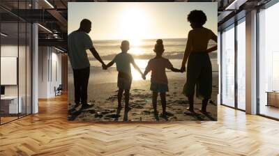 Rear view of african american family holding hands while looking at sunset over sea from beach shore Wall mural