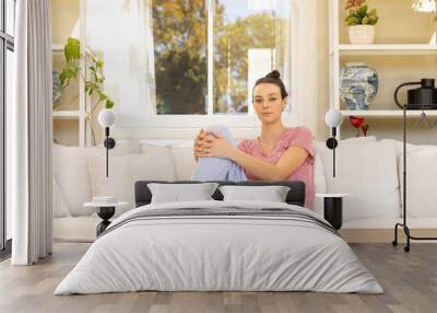 Sitting on couch, young woman relaxing at home in casual attire Wall mural