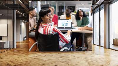 Smiling biracial disabled businesswoman looking over shoulder during meeting with colleagues Wall mural