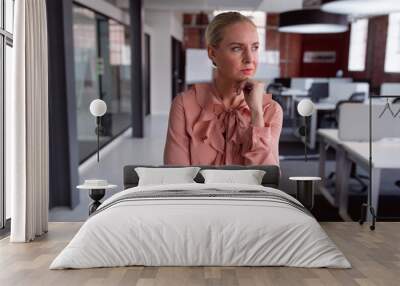 Thoughtful caucasian businesswoman standing in office with chin on hand, looking away Wall mural