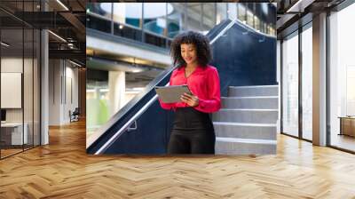 Using tablet, businesswoman standing on stairs in modern office building Wall mural