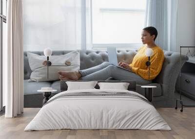 Woman using laptop on a sofa in living room Wall mural