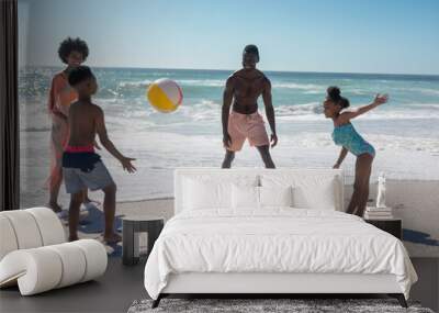 African american family enjoying summer holiday while playing with ball at beach on sunny day Wall mural