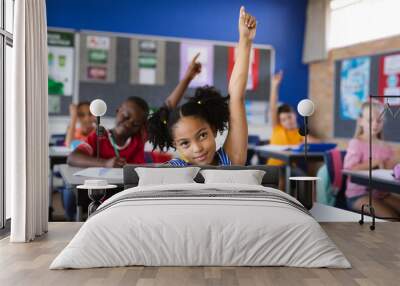 African american girl raising her hands while sitting on her desk in the class at school Wall mural