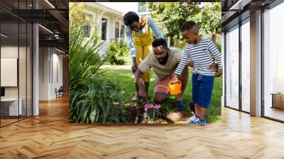 African american mother looking at father and son planting fresh flowers on land in yard Wall mural