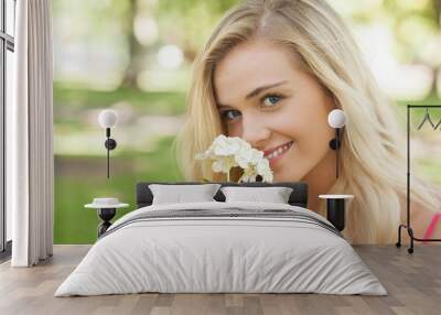 beautiful blonde woman smelling a flower sitting in a park Wall mural