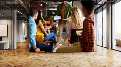 Caucasian casual businessman presenting to diverse colleagues using tablet in office Wall mural