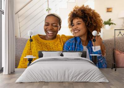 Cheerful multiracial young lesbian couple relaxing on sofa in living room Wall mural