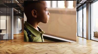 Close-up of thoughtful african american elementary schoolboy looking through window in classroom Wall mural