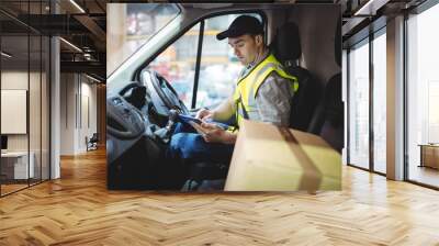 Delivery driver using tablet in van with parcels on seat Wall mural