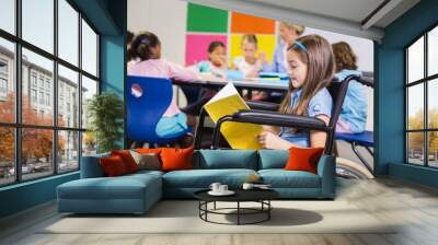 Disabled school girl on wheelchair reading a book in classroom Wall mural