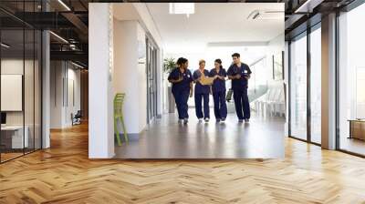 Diverse group of happy male and female doctors talking walking in hospital corridor, with copy space Wall mural