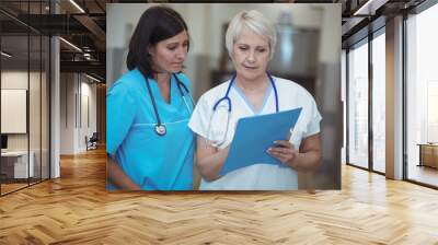 Female surgeon and nurse having discussion over file in corridor Wall mural