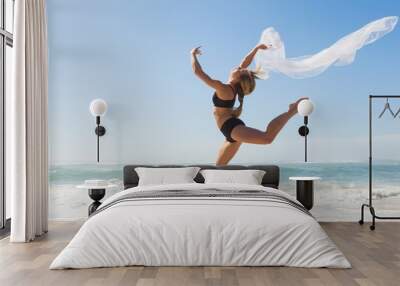 Fit blonde jumping gracefully with scarf on the beach Wall mural