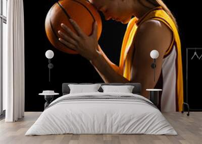 Focused young Caucasian female basketball player holds a basketball on a black background Wall mural