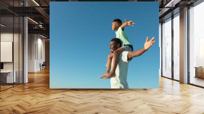 Happy african american boy on father's shoulders by copy space against clear blue sky Wall mural