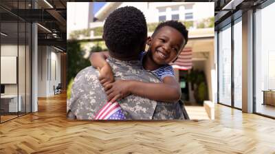 Happy african american boy with flag of america embracing army soldier father outside house Wall mural