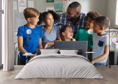 Happy african american young male teacher with multiracial elementary students using laptop Wall mural