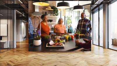 Happy diverse group of senior friends preparing meal in sunny kitchen at home Wall mural