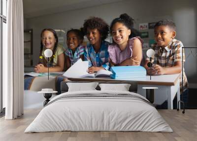 Happy multiracial elementary school students sitting at desk in classroom Wall mural