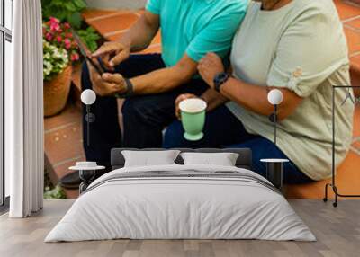 High angle view of biracial senior man showing digital pc to wife holding cup while sitting on steps Wall mural