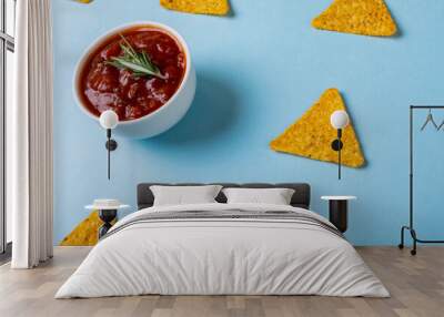 High angle view of red sauce with rosemary by nacho chips over blue background Wall mural