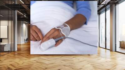 Midsection of mixed race female patient in hospital bed wearing fingertip pulse oximeter and iv tube Wall mural