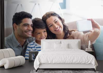 Parents and son taking a selfie from mobile phone in living room Wall mural