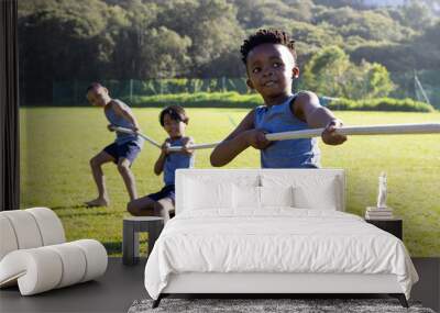 Playing tug of war, multiracial boys enjoying outdoor activity at school field Wall mural