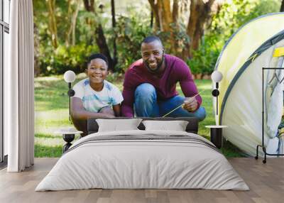 Portrait of african american father with son having fun and pitching tent in garden Wall mural