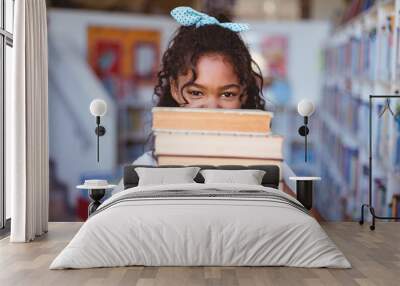 Portrait of happy african american schoolgirl carrying stack of books in school library Wall mural