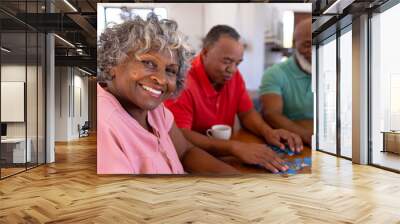 Portrait of smiling multiracial senior woman solving jigsaw puzzle with male friends in nursing home Wall mural