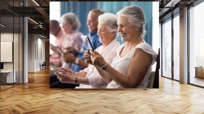 Row of smiling senior people sitting on chairs using digital Wall mural