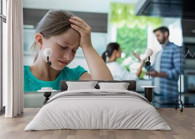 Sad girl leaning on chair while parents arguing in background Wall mural