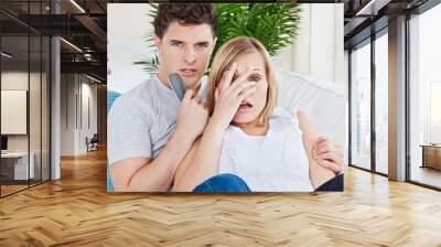 Scared couple watching a horror movie lying on the sofa Wall mural