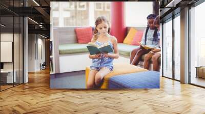 School kids sitting on sofa and reading book in library Wall mural