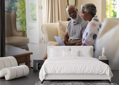 Senior african american couple sitting on sofa using laptop and talking Wall mural