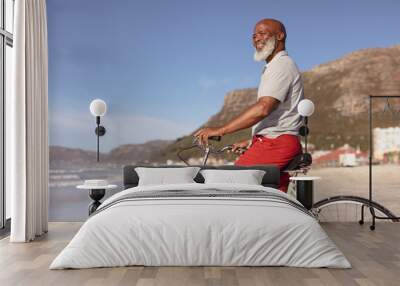 Senior african american man sitting on bicycle smiling on the beach Wall mural