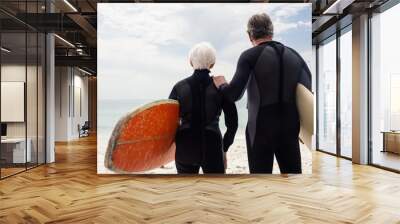 Senior couple in wetsuit holding surfboard on beach Wall mural